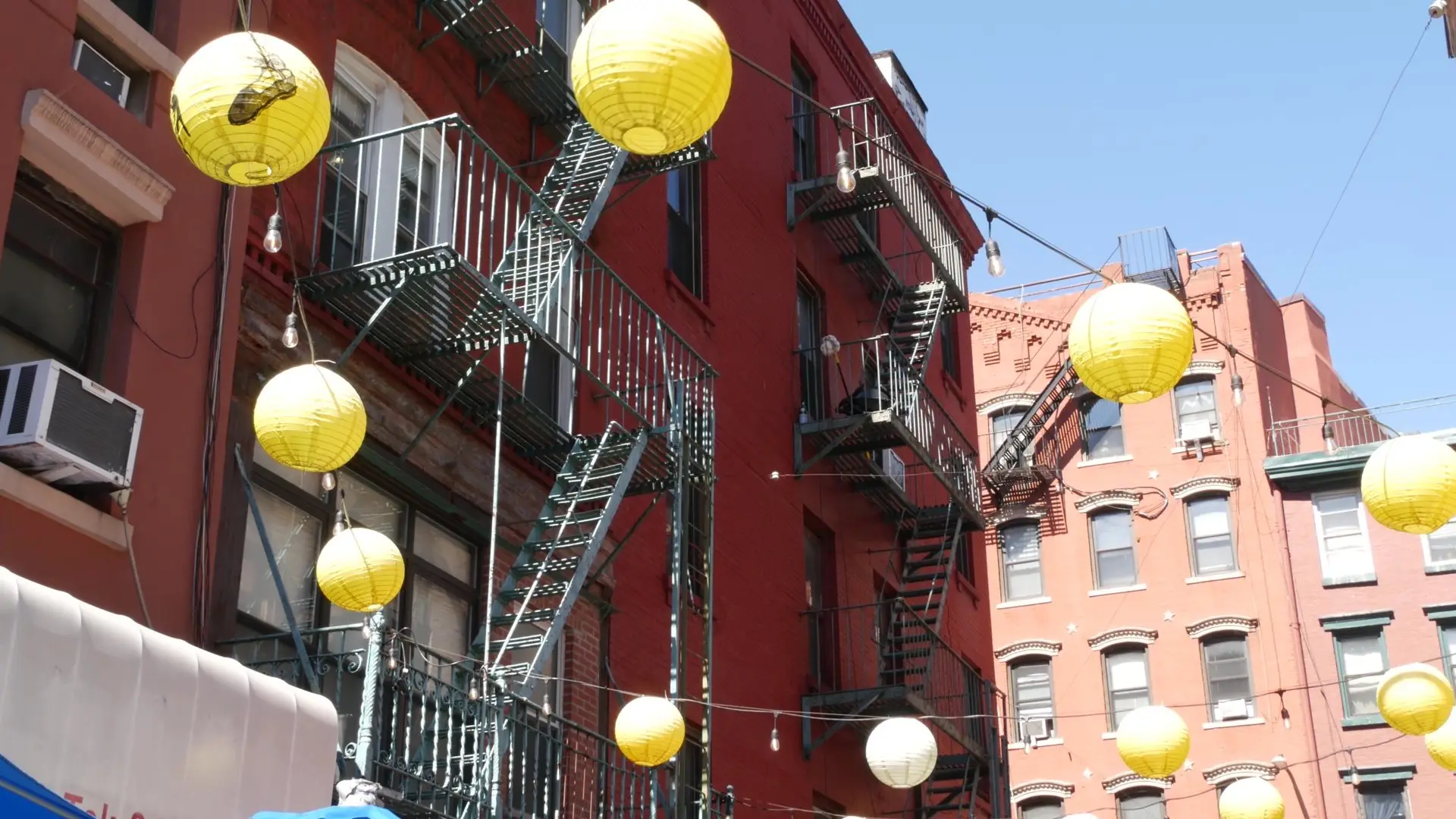 Paper lanterns strung between red-brick tenements and fire escapes in Manhattan's Chinatown